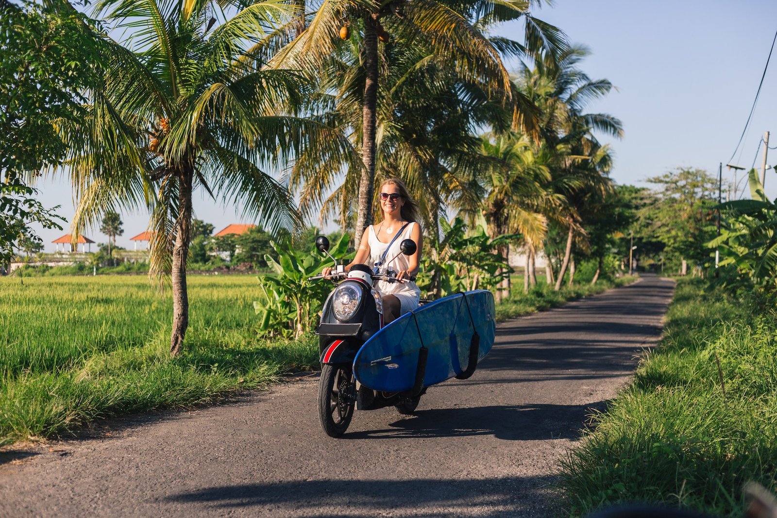 young-woman-riding-scooter-with-surfing-board.jpg